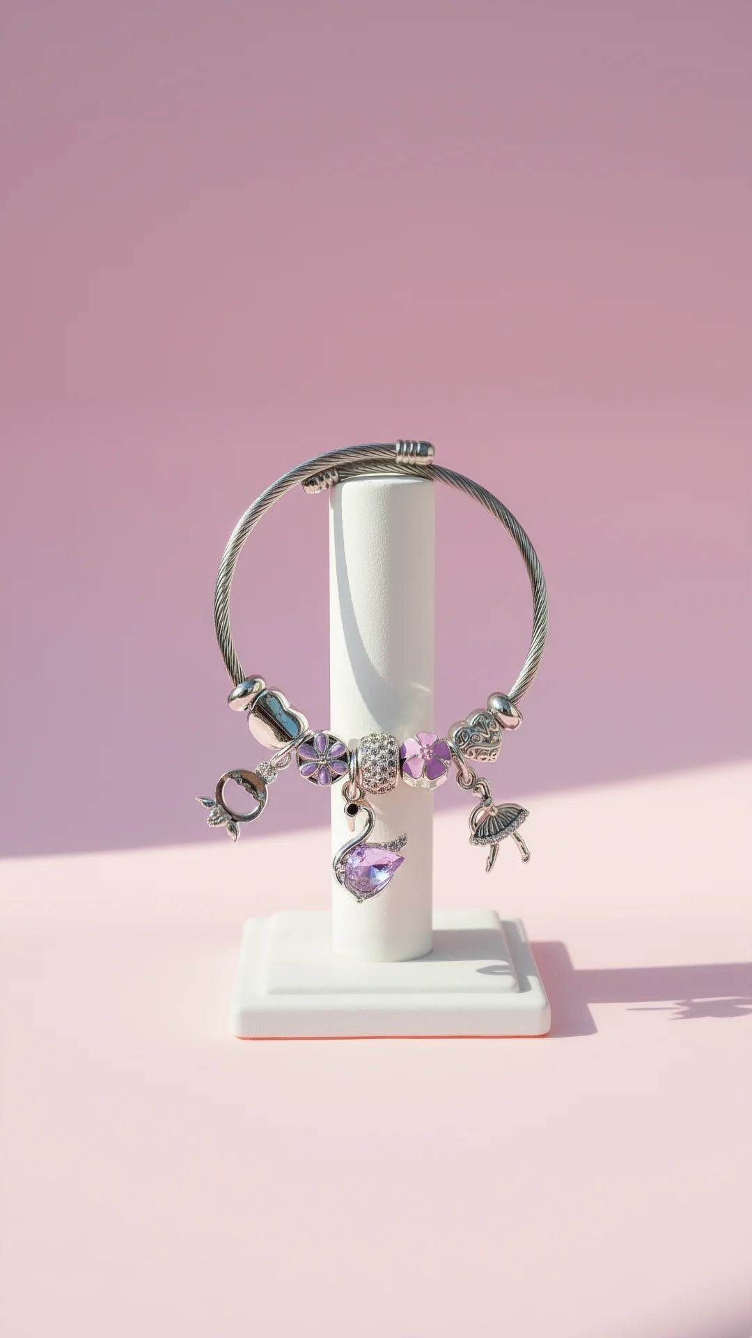 Bracelet with charms on a white stand against a pink background