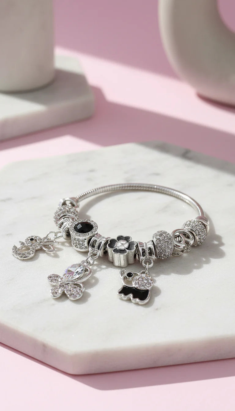 Silver bracelet with charms on a marble surface with a pink background