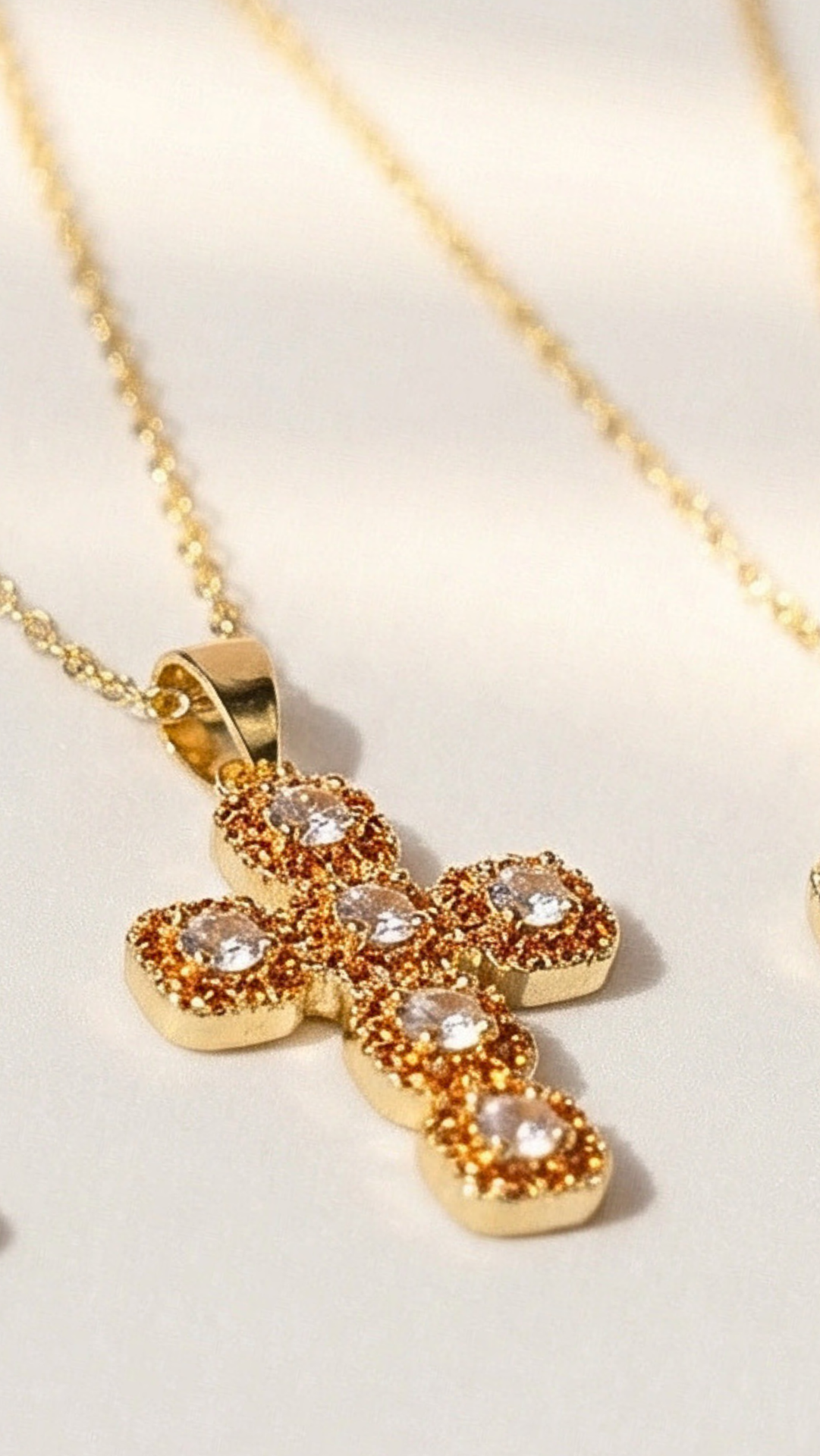 Gold cross pendant with embedded stones on a light background