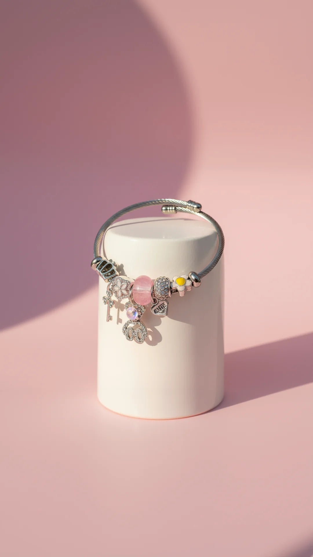 Bracelet with charms on a cylindrical white container against a pink background