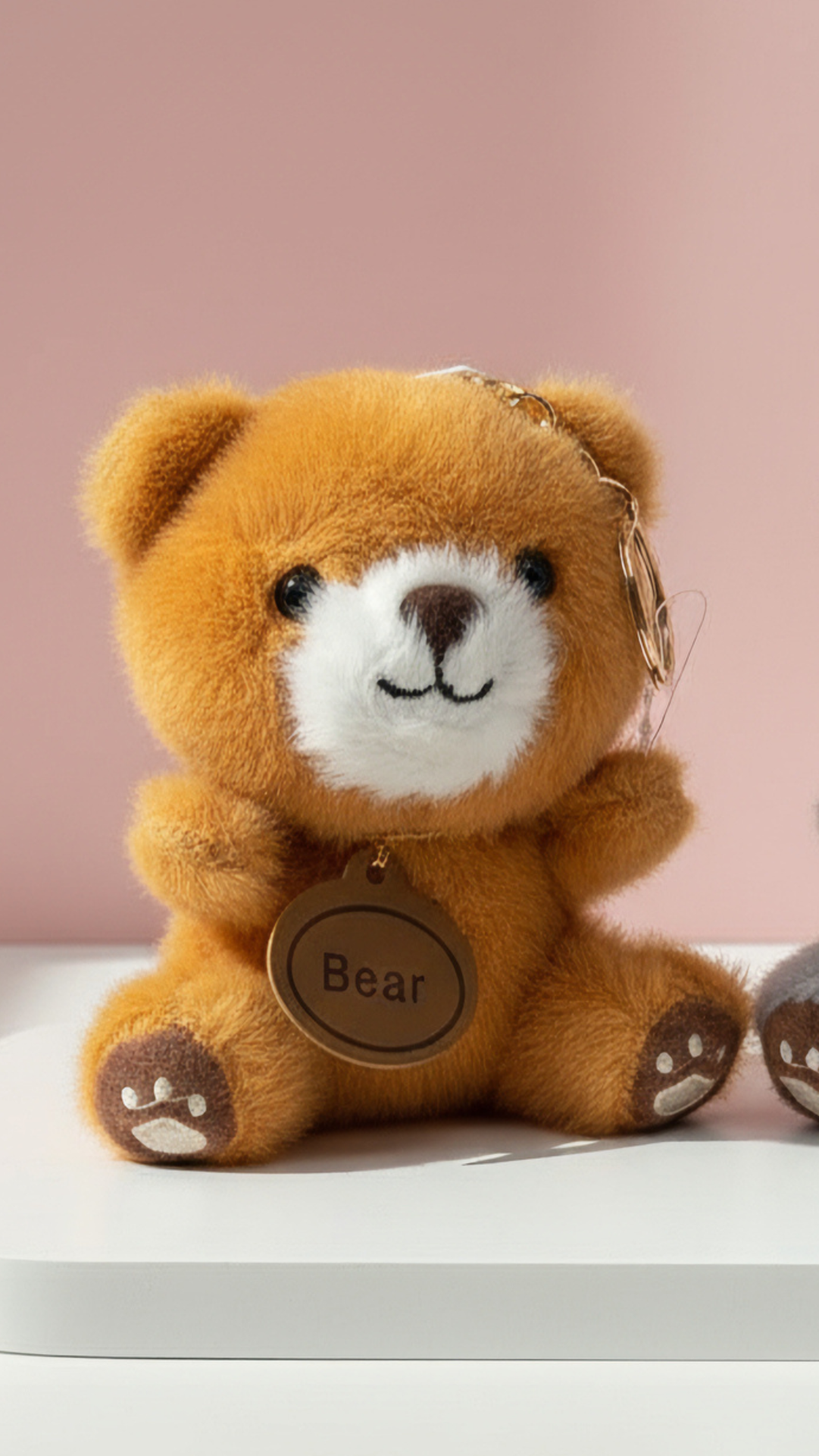 Brown teddy bear keychain with 'Bear' tag on a light pink background