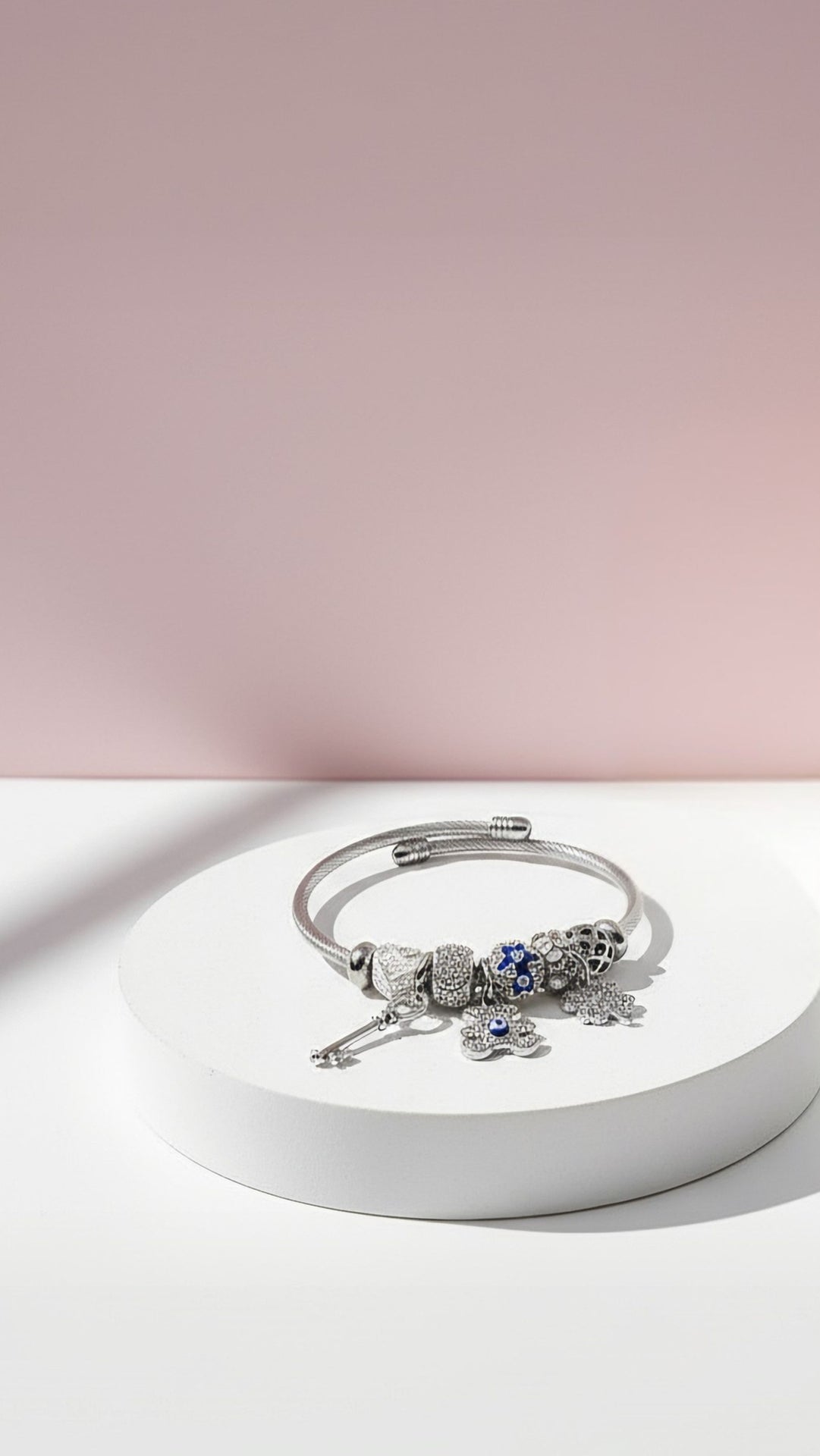 Silver bracelet with a lizard charm on a white platform against a pink background