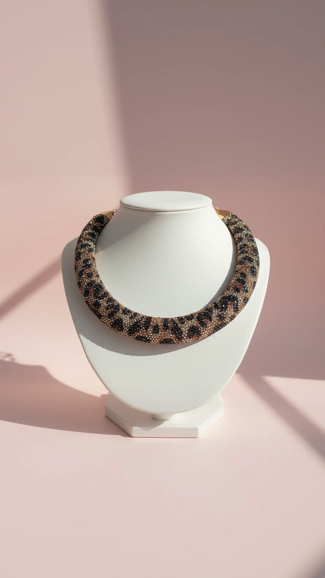 Leopard print necklace on a white stand against a pink background