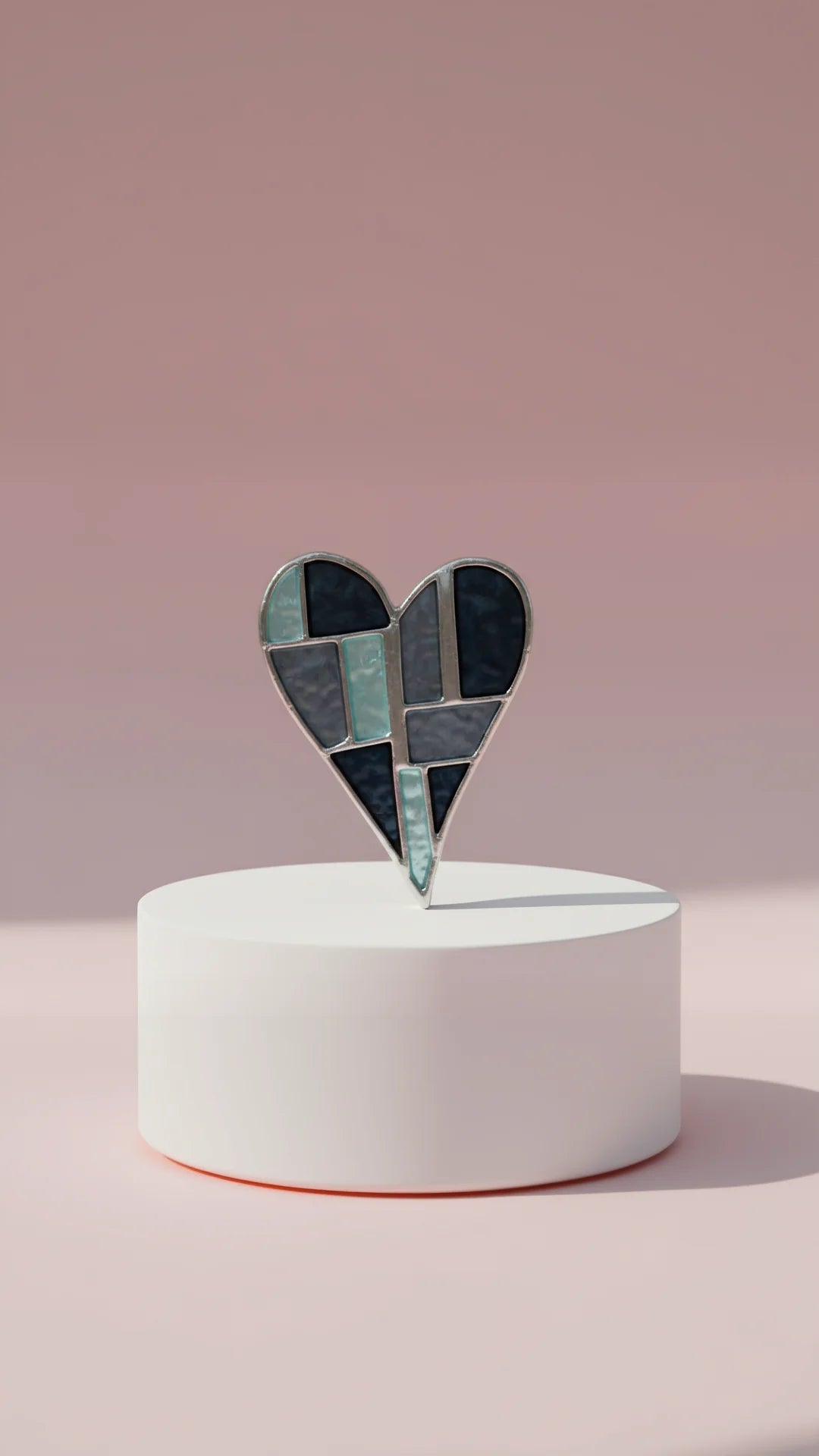 Heart-shaped multicolor brooch on a white pedestal against a pink background
