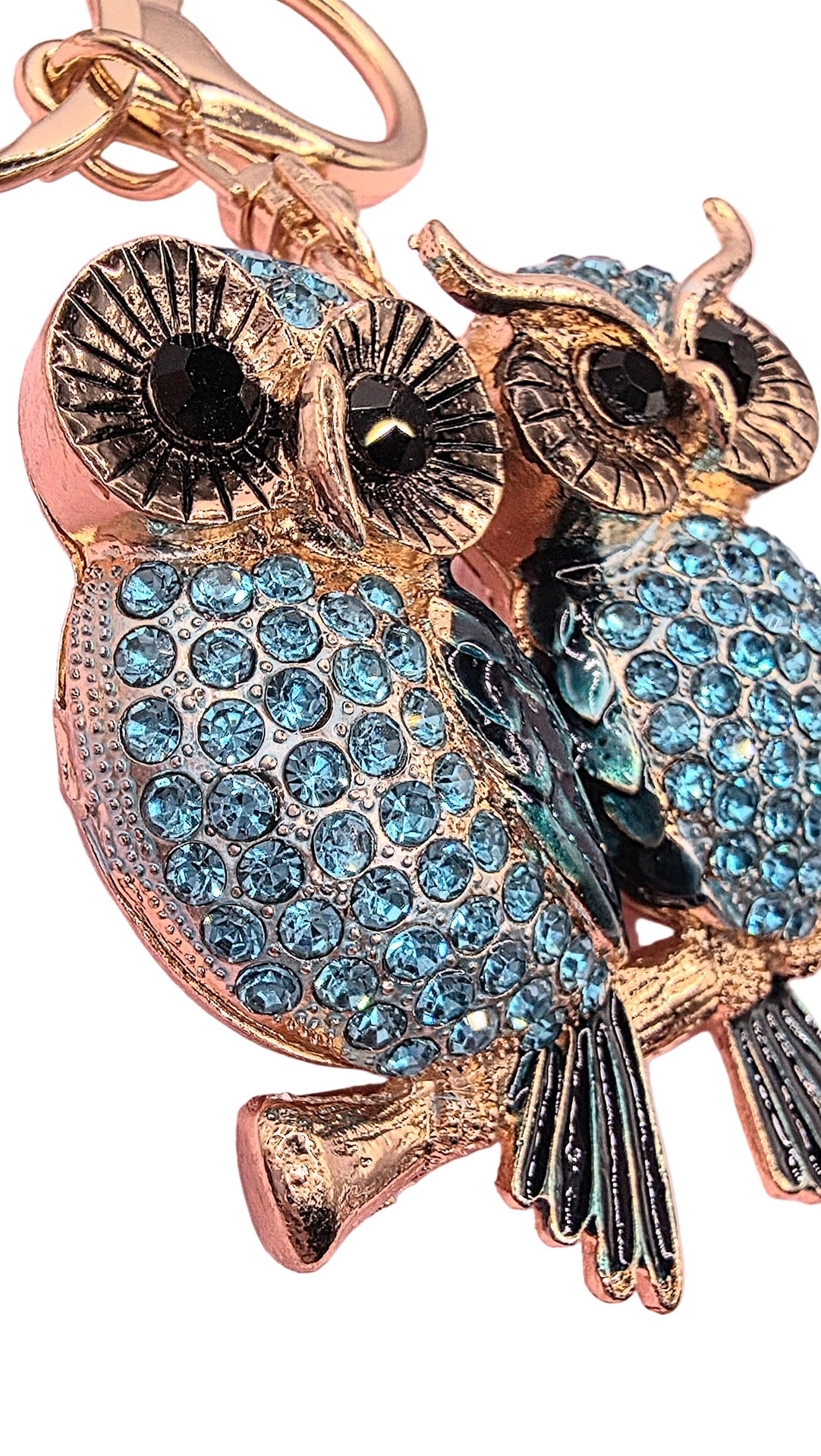 Gold owl keychain with blue gemstones on a pink background