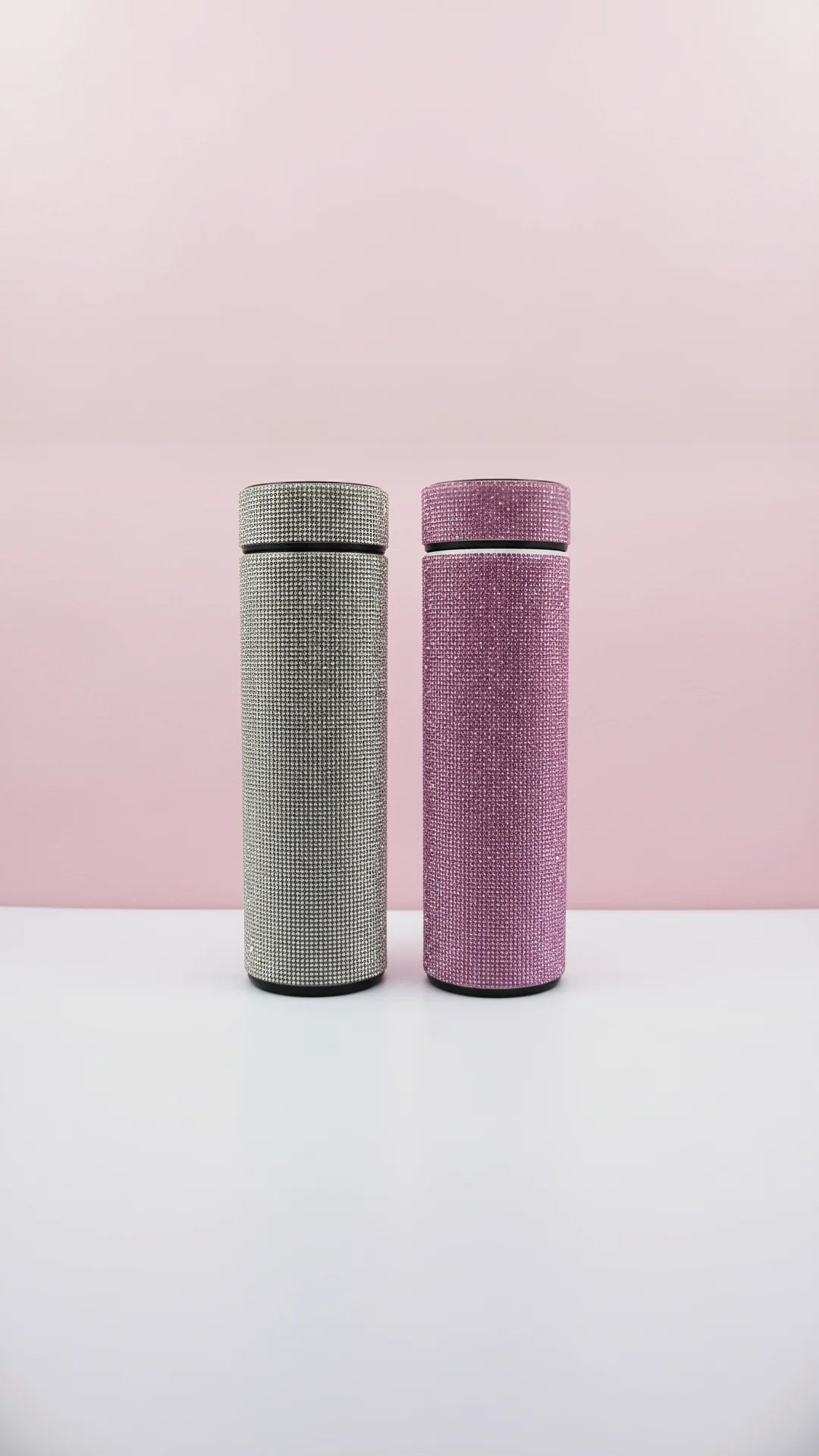 Two textured bottles, one gray and one pink, on a white surface with a pink background.