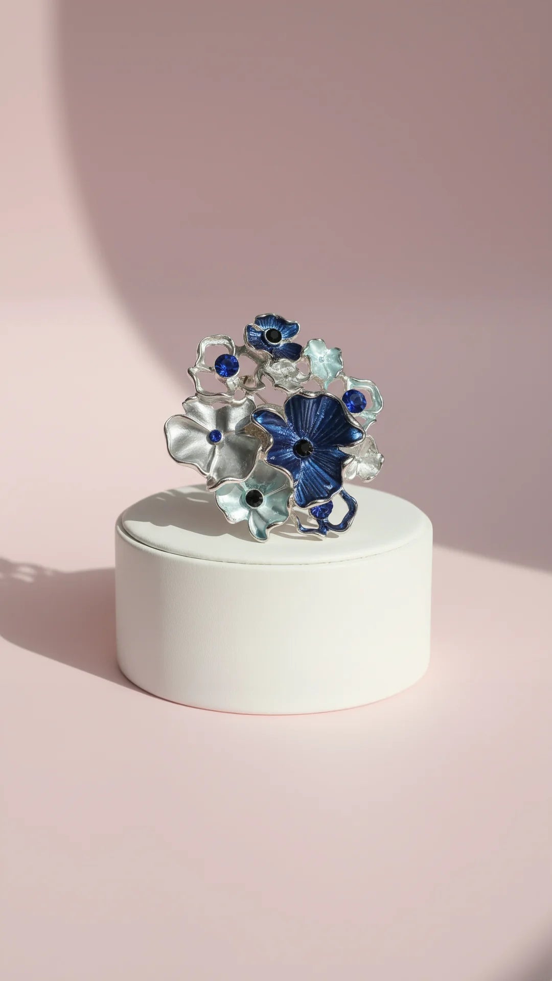 Floral gray & navy brooch displayed on a white base against a pink background