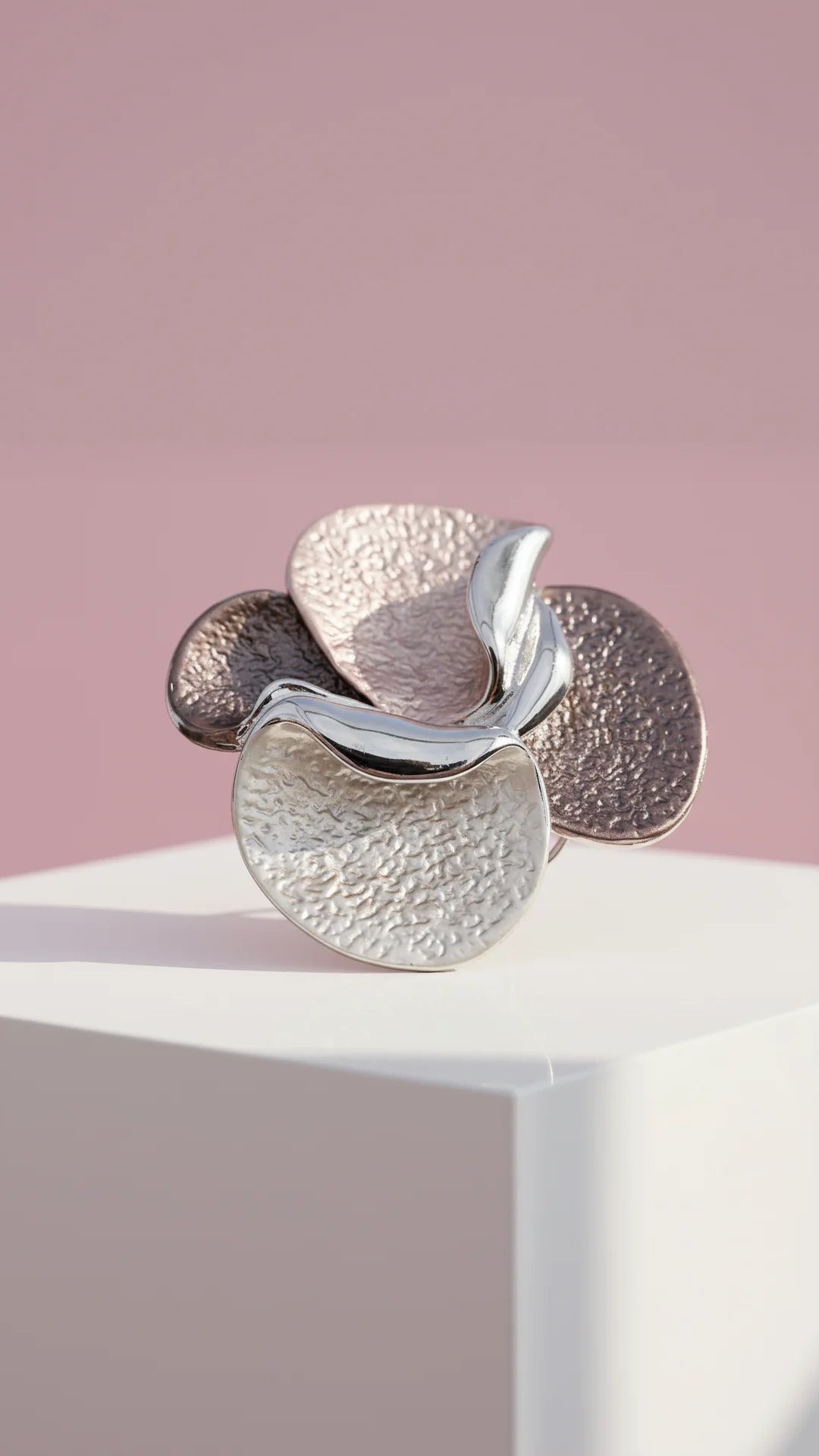 Silver flower-shaped brooch on a white stand with a pink background