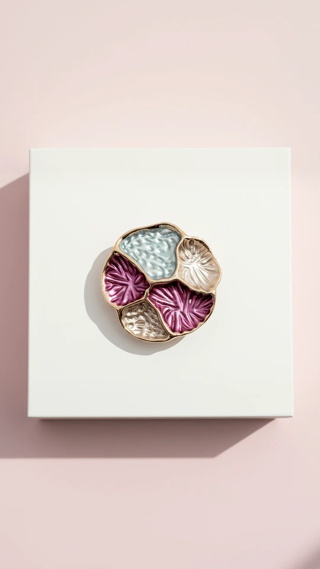 Decorative brooch with floral design on a white box against a pink background