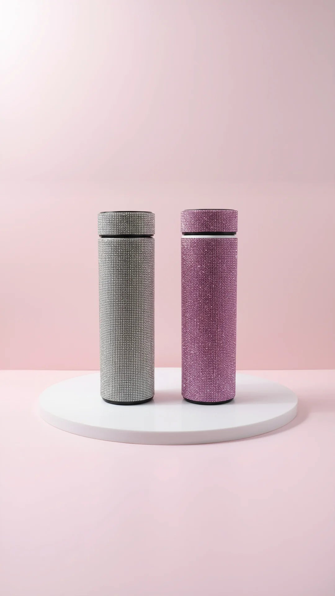 Two textured bottles, one gray and one pink, on a white platform with a pink background