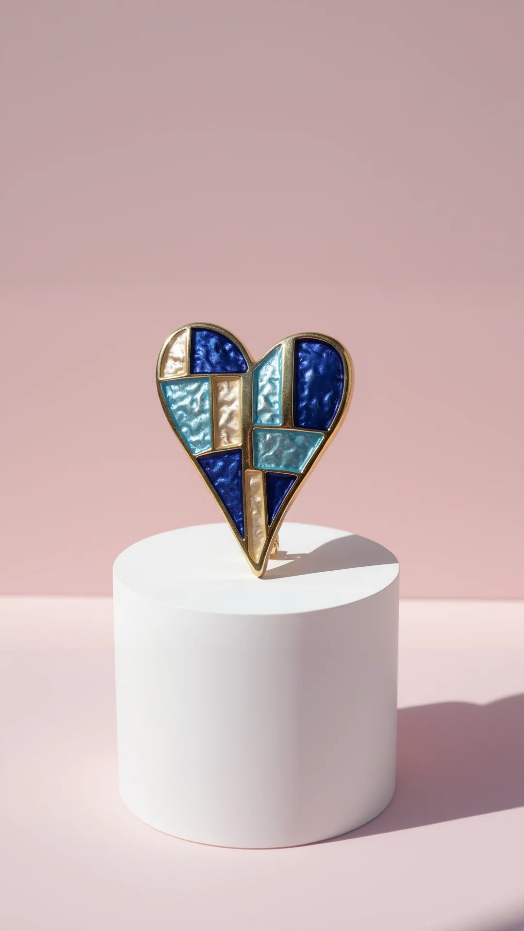 Heart shaped multicolors brooch on a white display against a pink background.