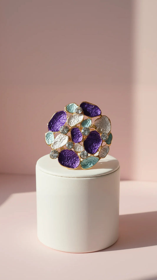 Multicolored brooch on a white cylindrical stand against a pink background