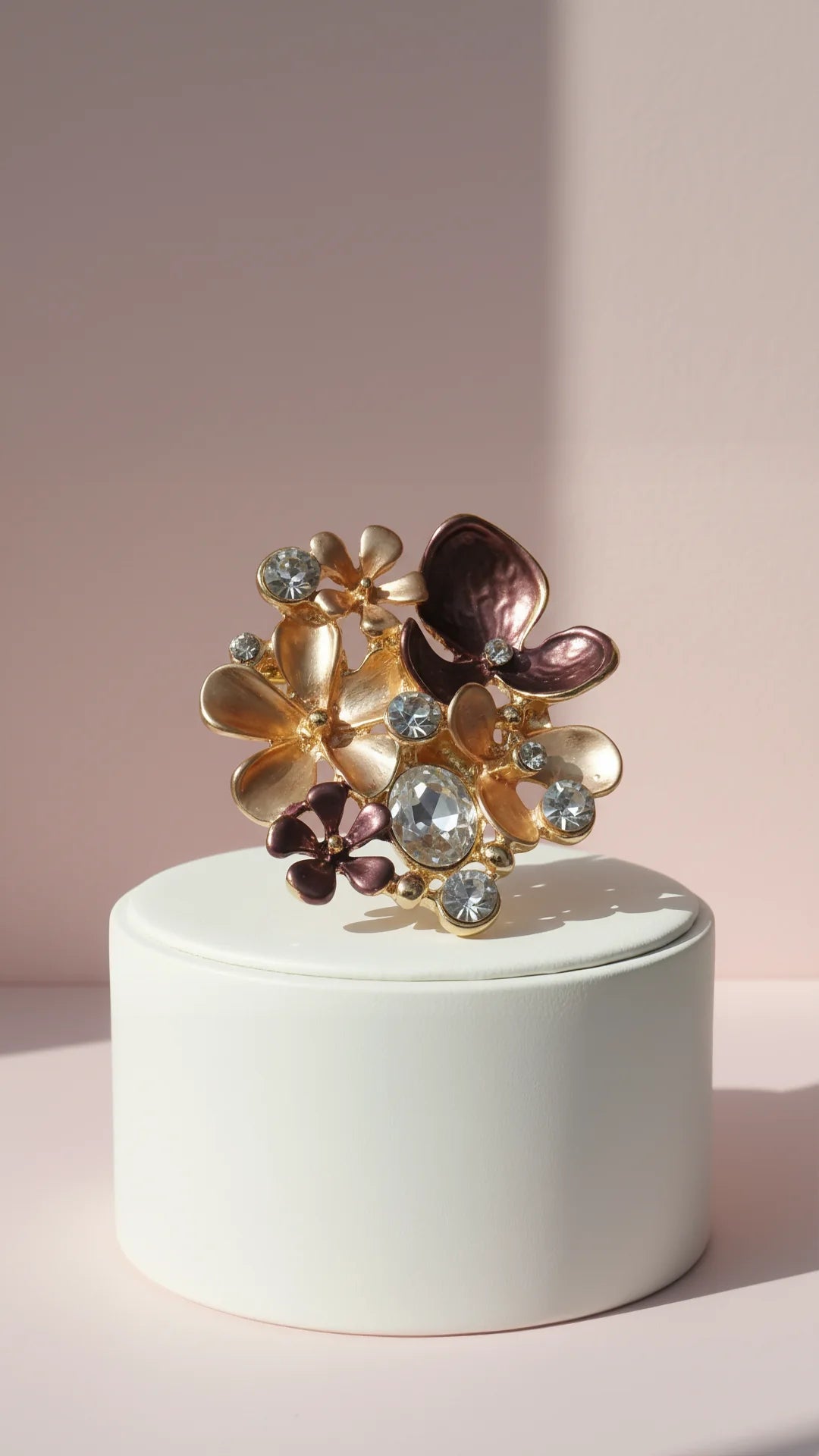 Multicolored floral brooch on a white pedestal against a light pink background