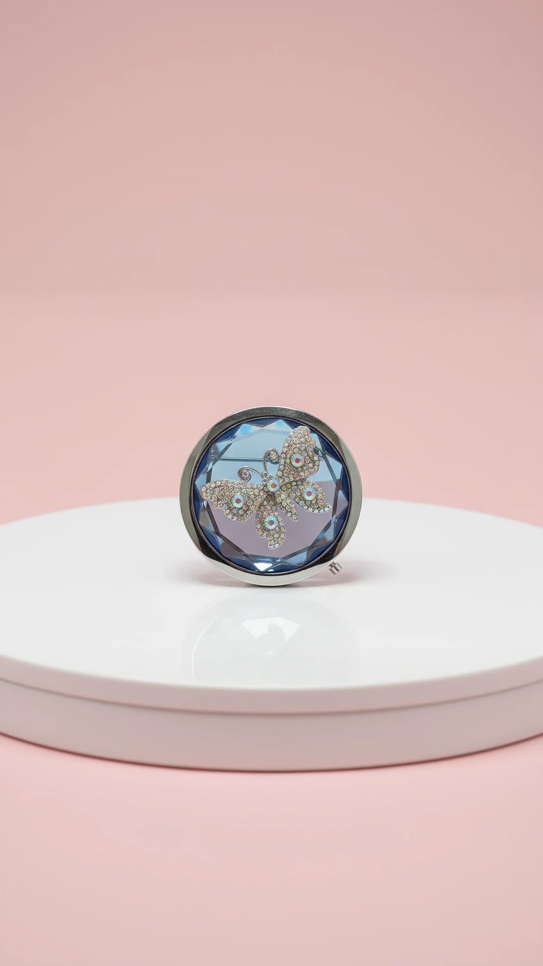 Round compact mirror with floral design on a white platform against a pink background