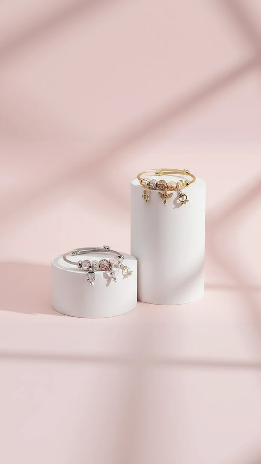 Two bracelets on white cylindrical stands against a pink background