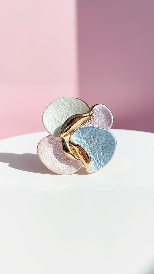 Gold and silver brooch on a white surface with a pink background