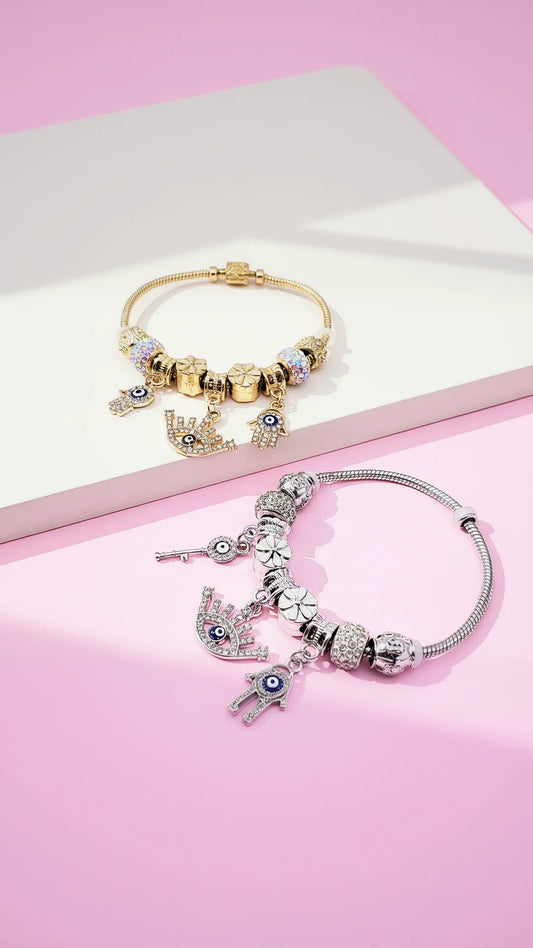 Two evil eye golden and silver bracelets with charms displayed on a white surface with pink background