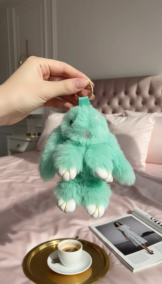 Green plush keychain held by a hand over a bed with a cup and magazine.