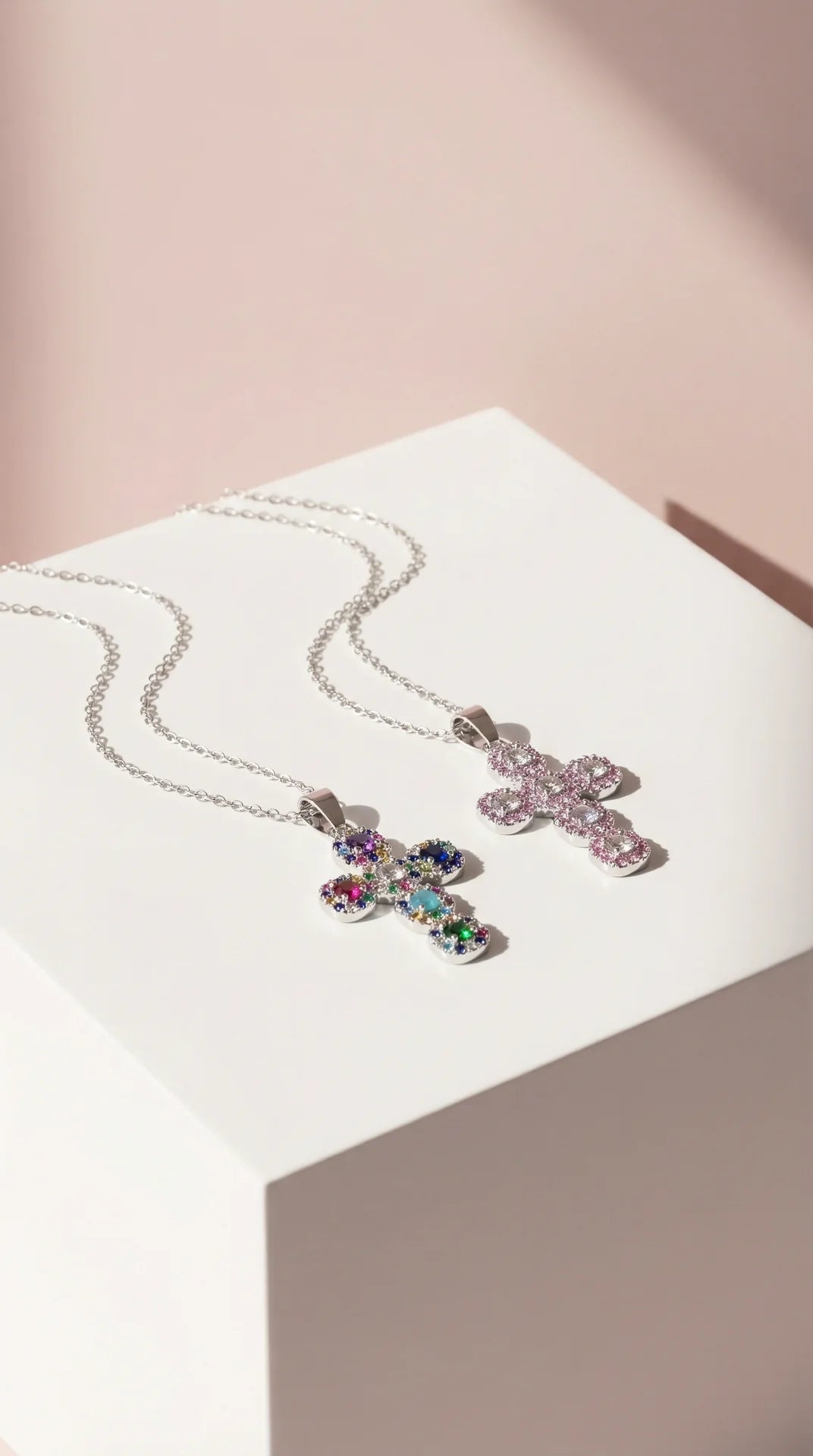 Two cross-shaped pendants on a white surface with a pink background