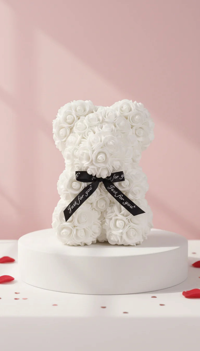 White rose teddy bear with black bow, displayed on a white circular table against a pink background.