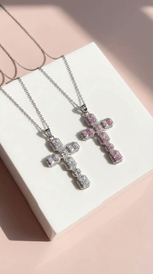 Two cross-shaped necklaces with pink and clear gemstones on a white card.