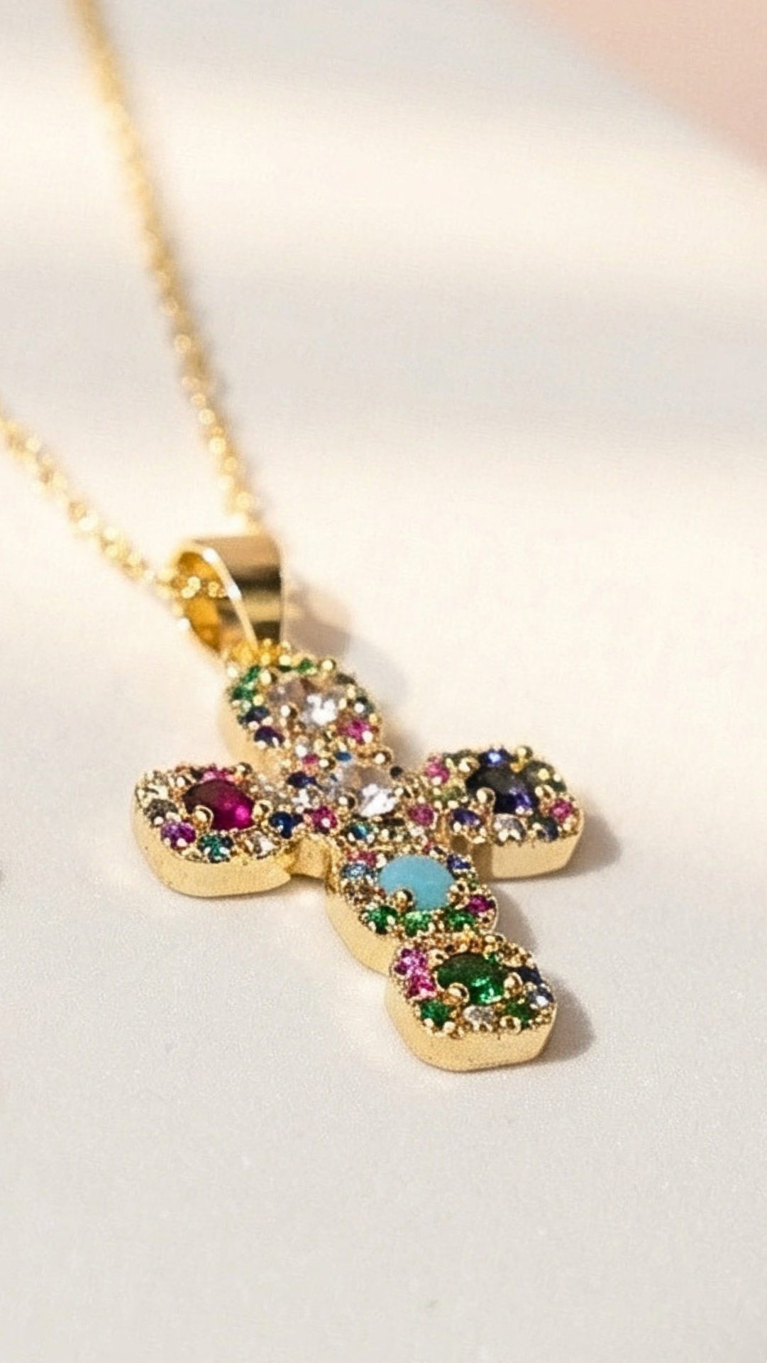 Gold cross necklace with colorful gemstones on a light background