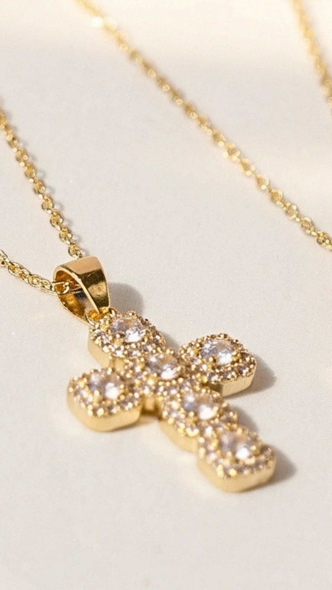 Gold cross necklace with clear stones on a light background
