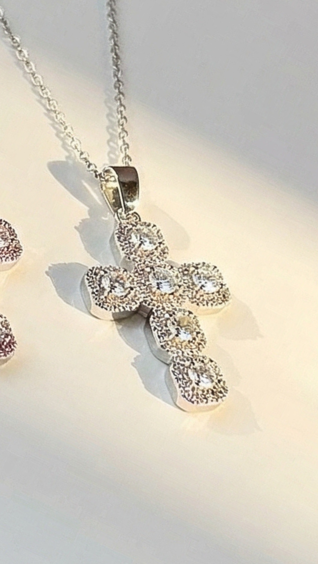 Silver cross pendant necklace with clear stones on a light background