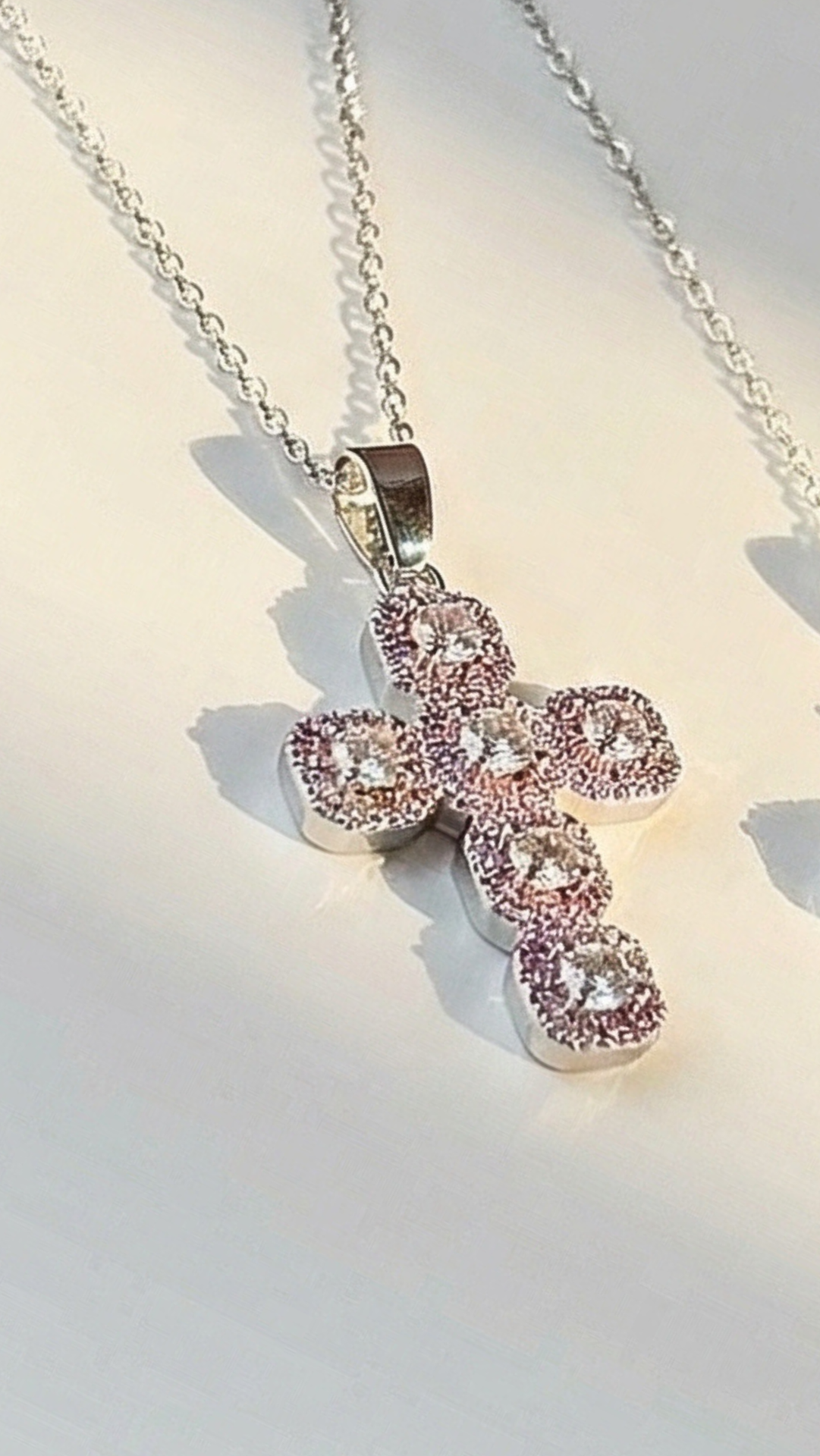 Silver cross pendant with pink gemstones on a chain against a light background