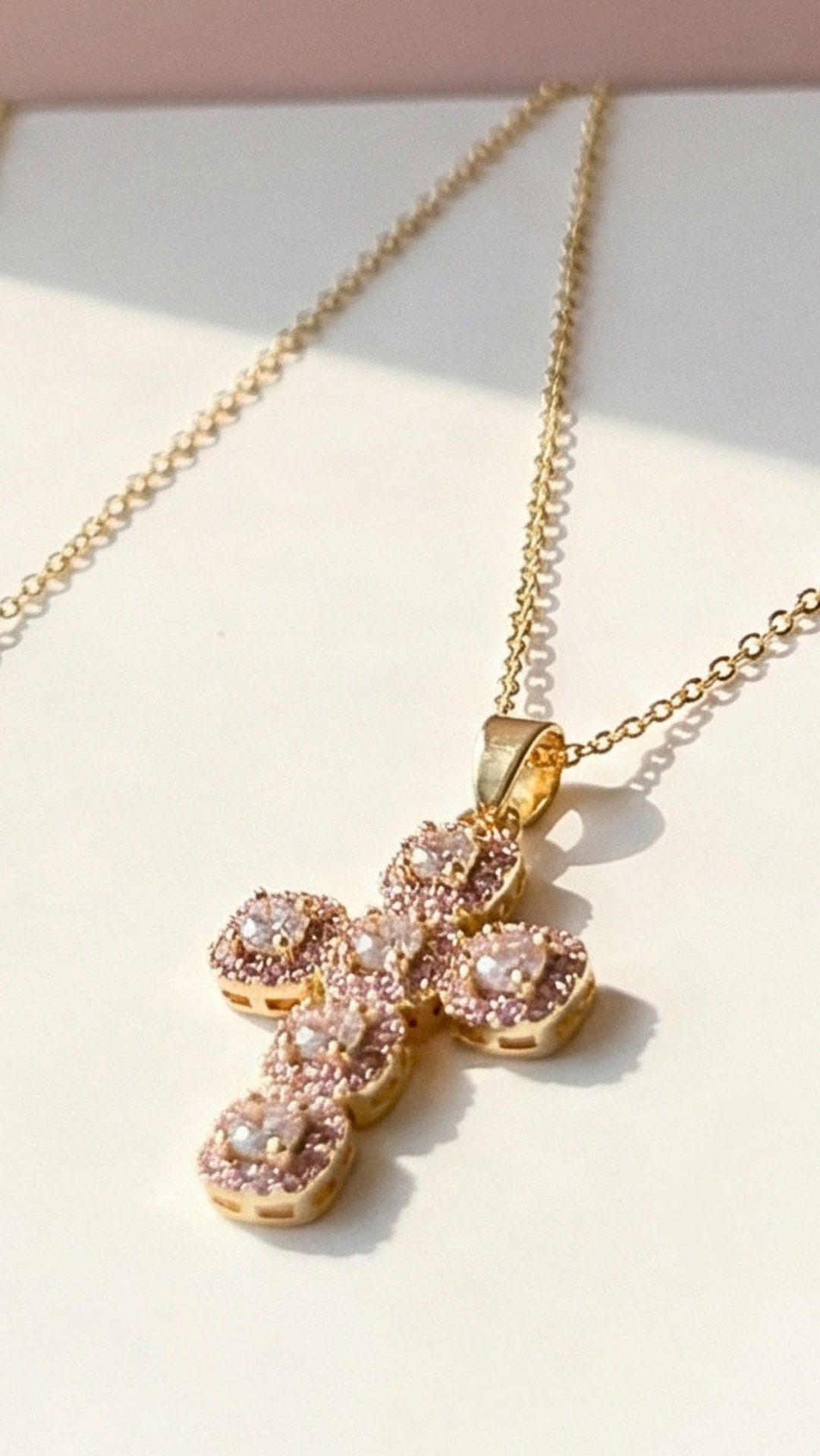 Gold cross necklace with pink gemstones on a light background