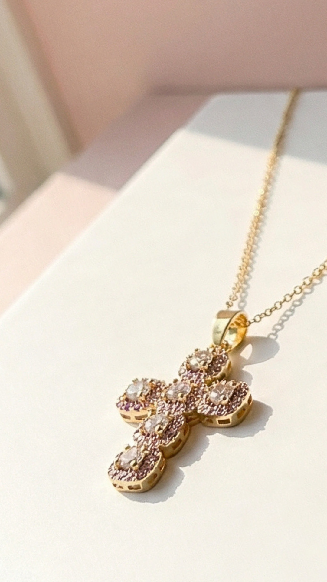 Gold cross necklace with pink gemstones on a light background