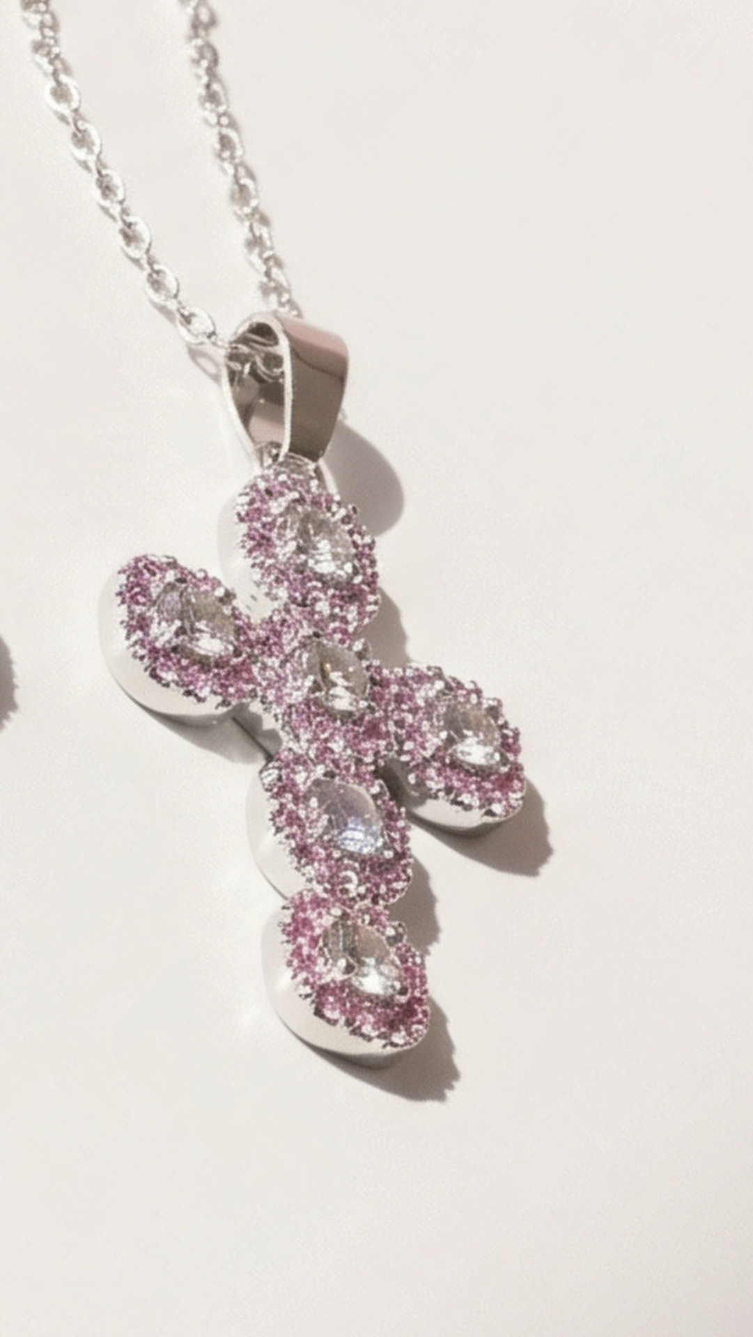Pink cross-shaped pendant on a chain against a light background