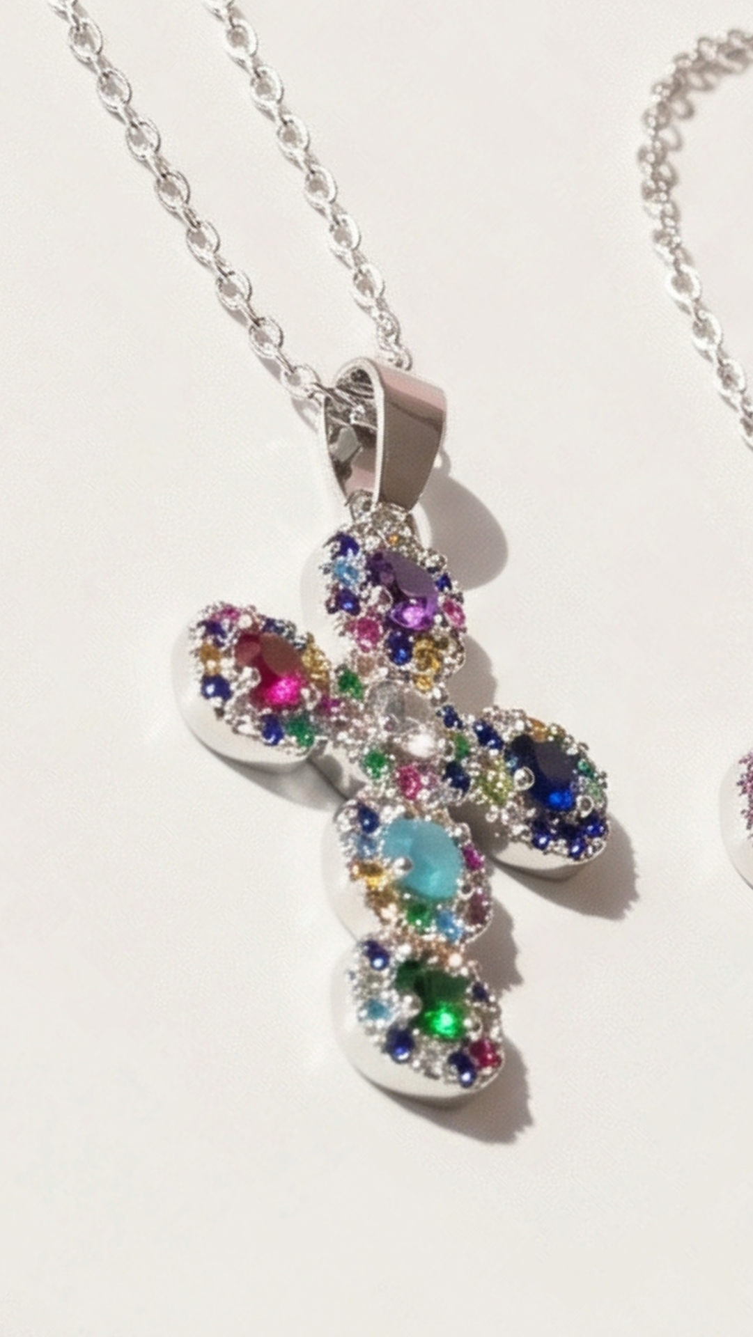 Multicolor gemstone cross pendant with silver finish displayed on a white surface.