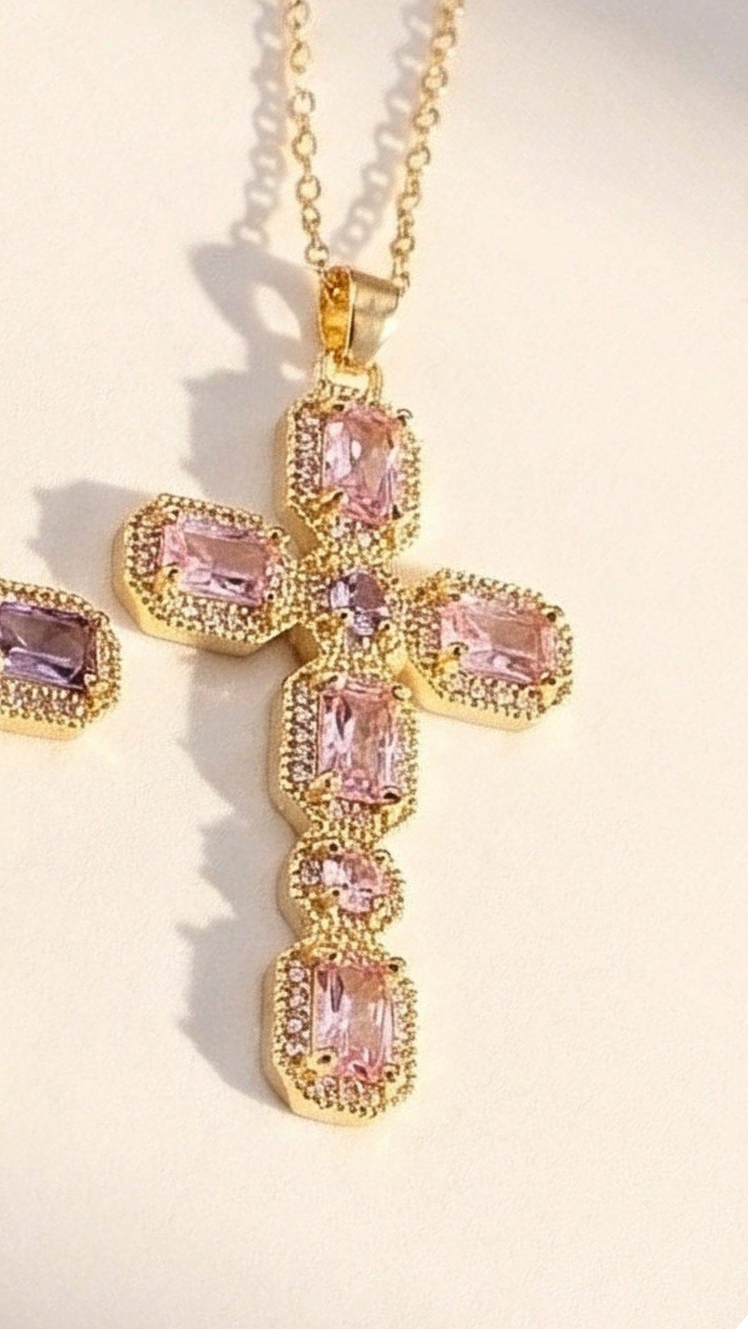 Gold cross pendant with pink gemstones on a light background