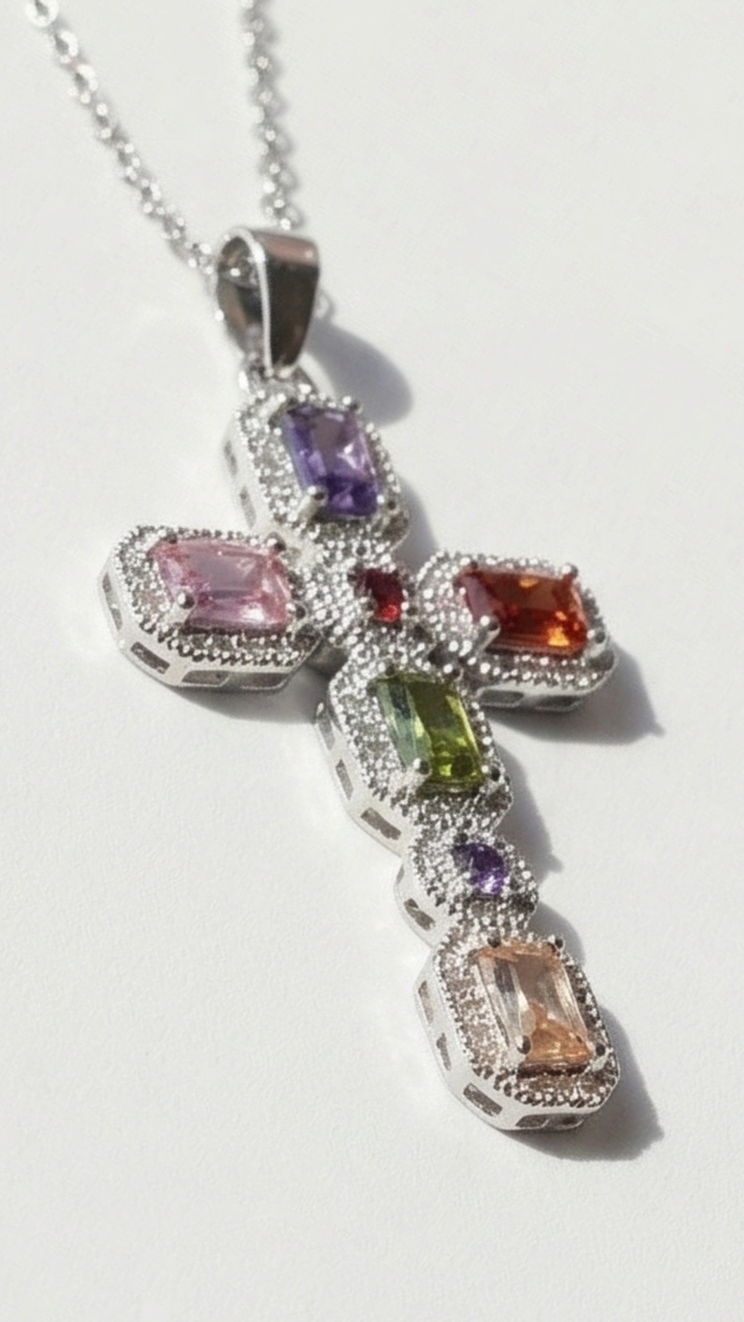 Multicolored gemstone cross pendant on a white background