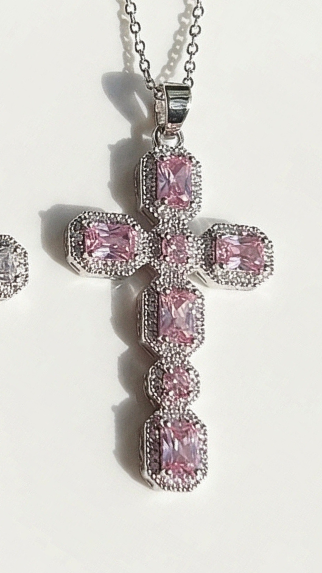 Pink cross-shaped pendant with clear stones on a white background