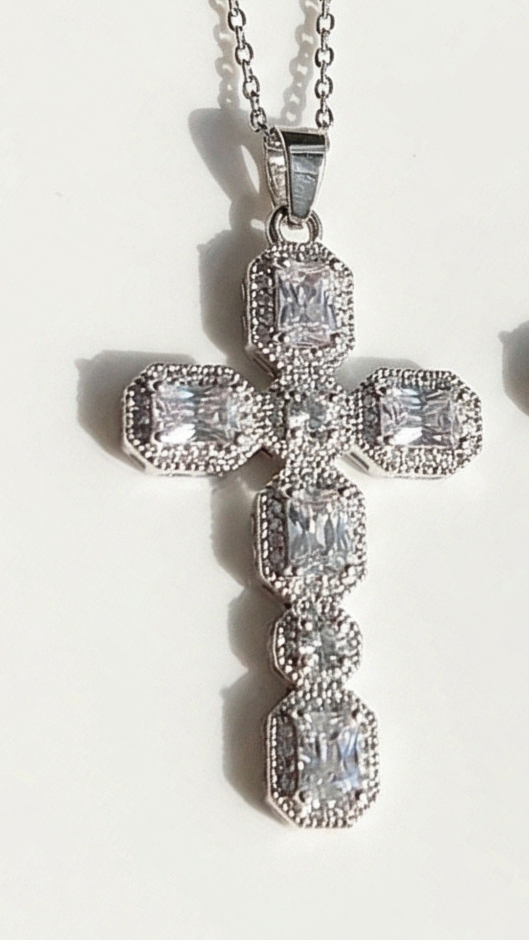 Silver cross-shaped pendant with clear stones on a white background
