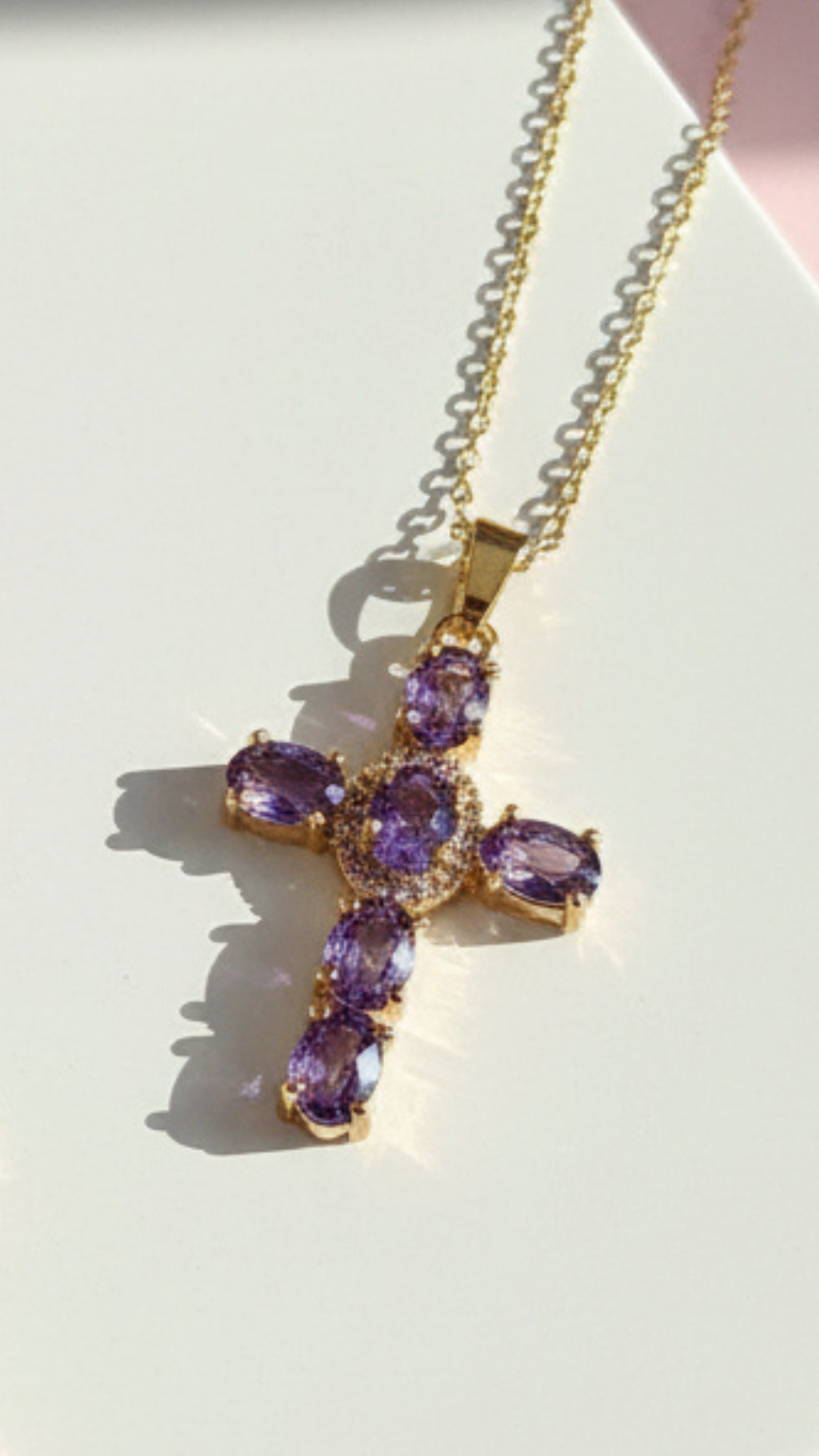 Golden cross pendant with light purple crystals displayed on a white surface