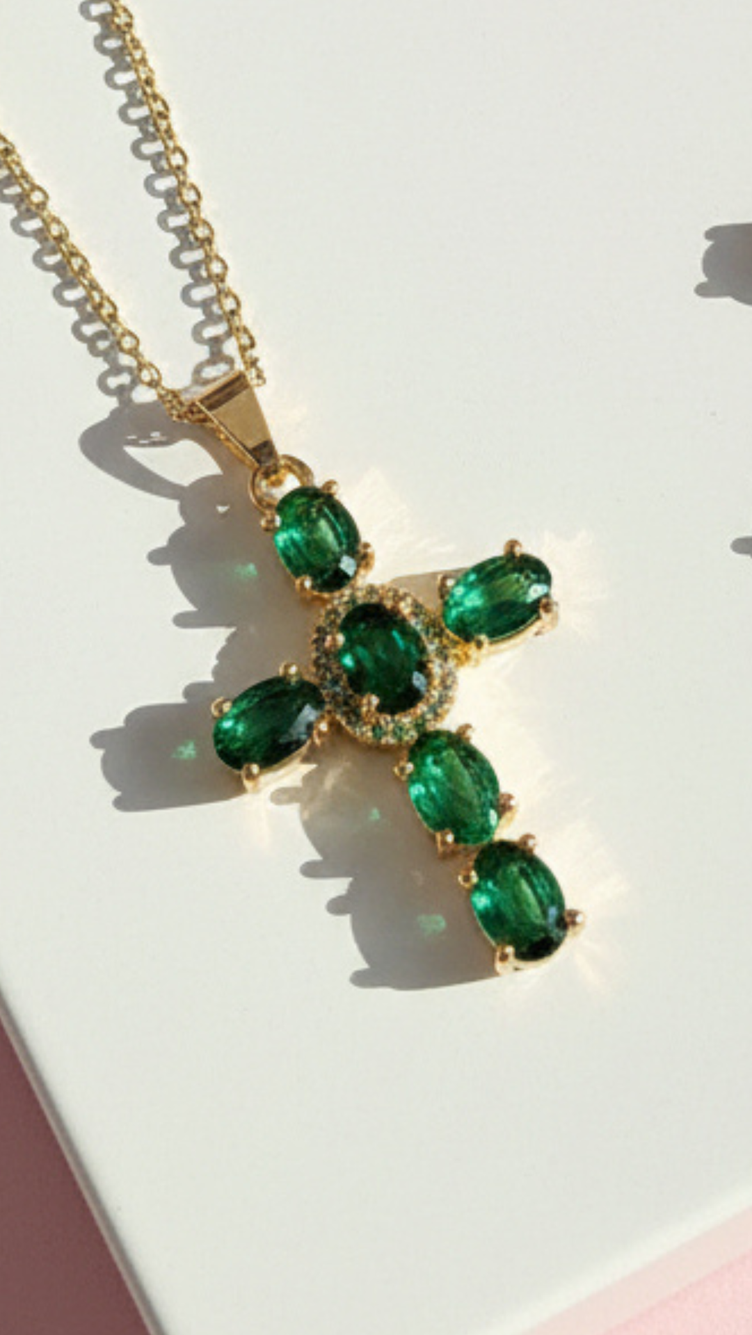 Gold necklace with green gemstone pendant on a light background