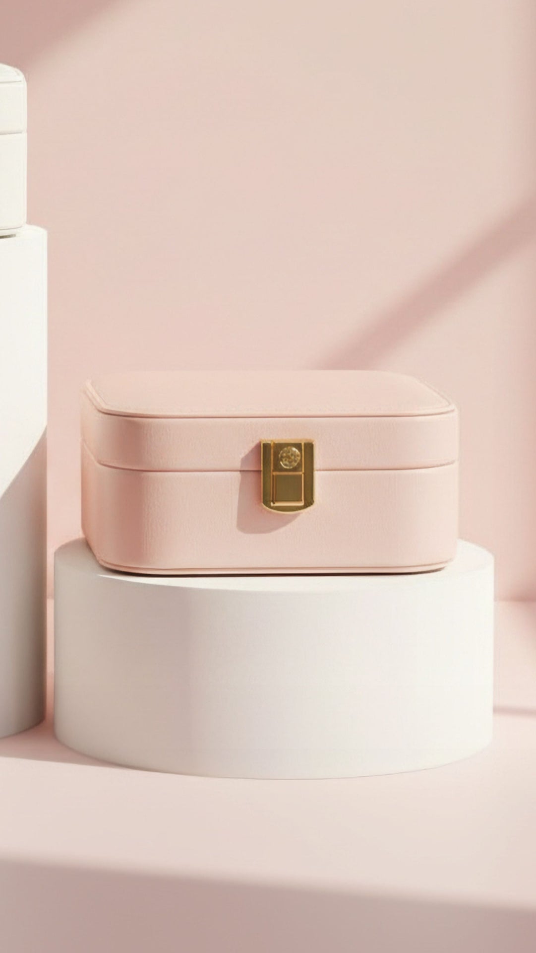 Pink jewelry box with a gold clasp on a white pedestal against a pink background