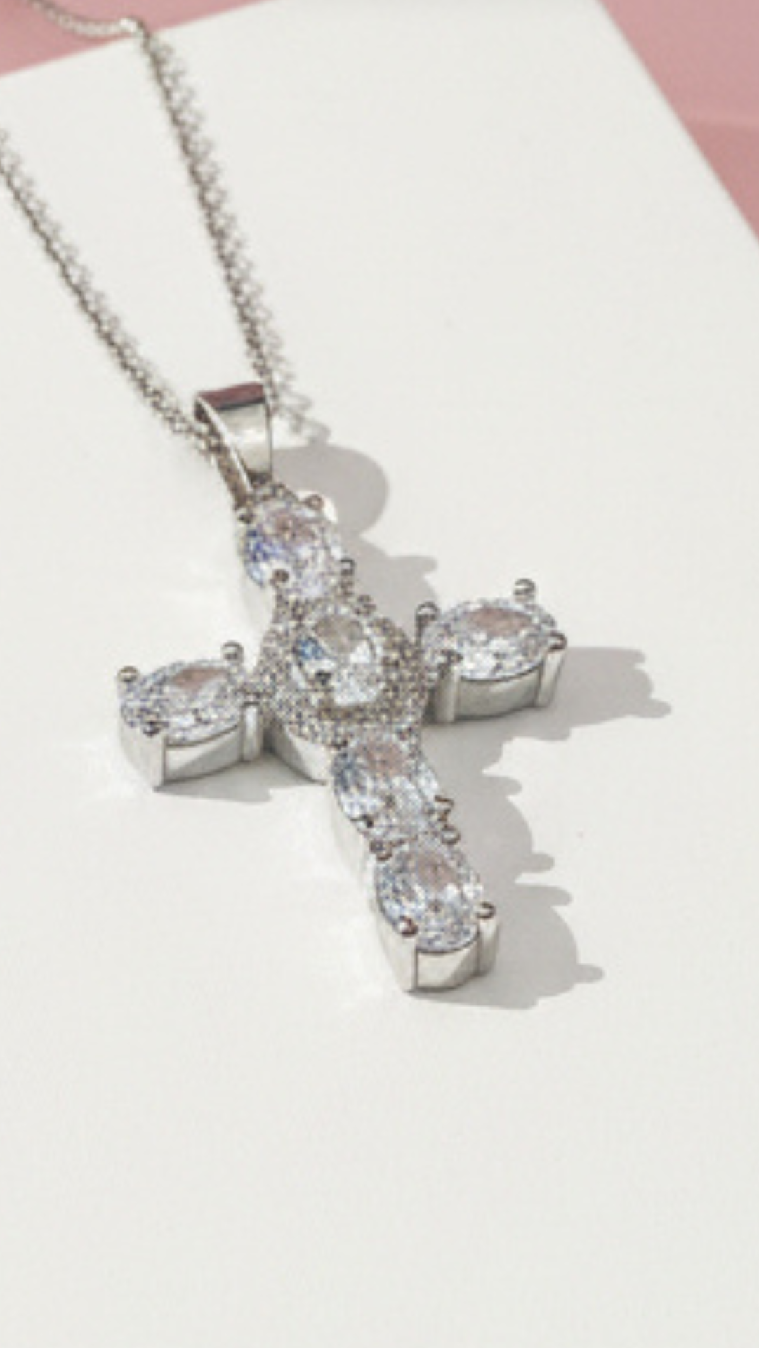 Silver cross pendant with clear stones on a white surface