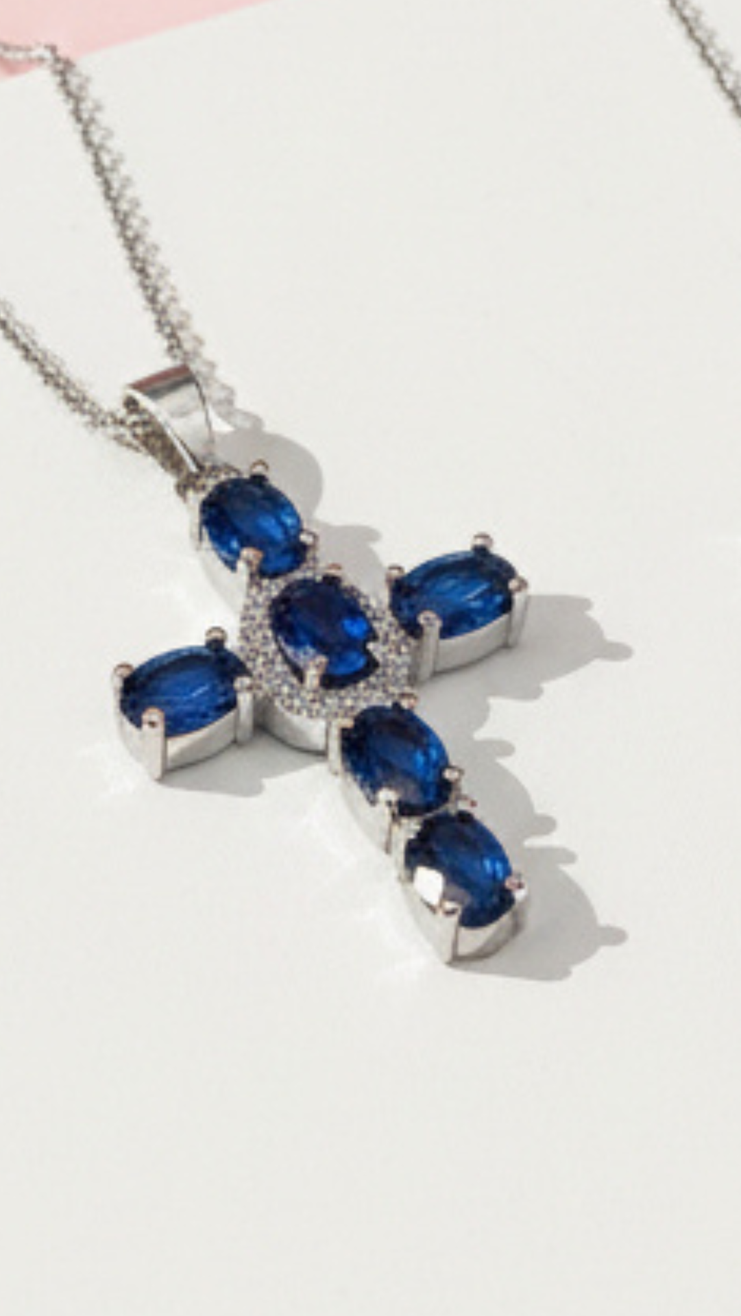 Silver cross pendant with navy crystal on a white surface