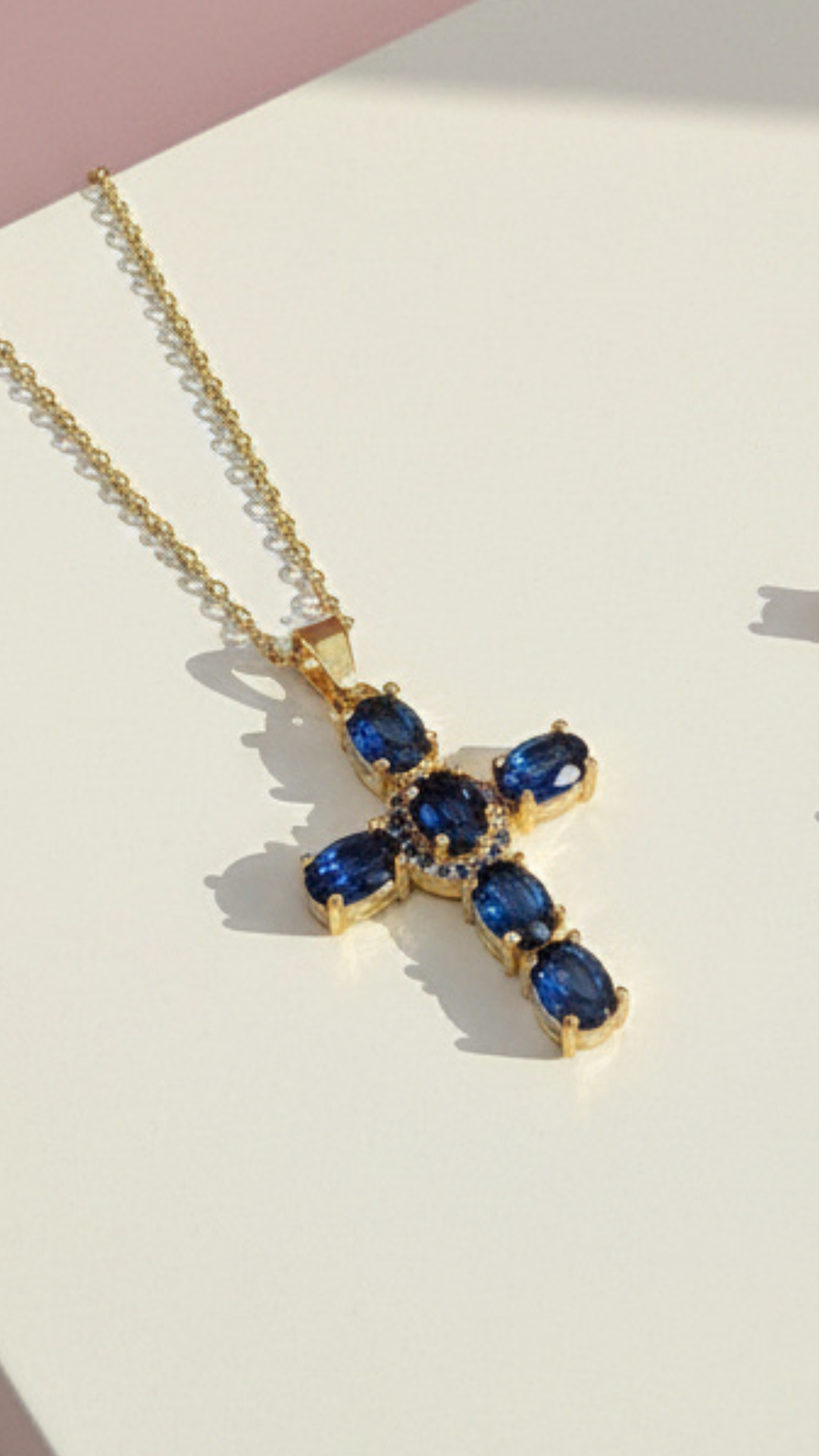 Gold necklace with a blue gemstone cross pendant on a light background