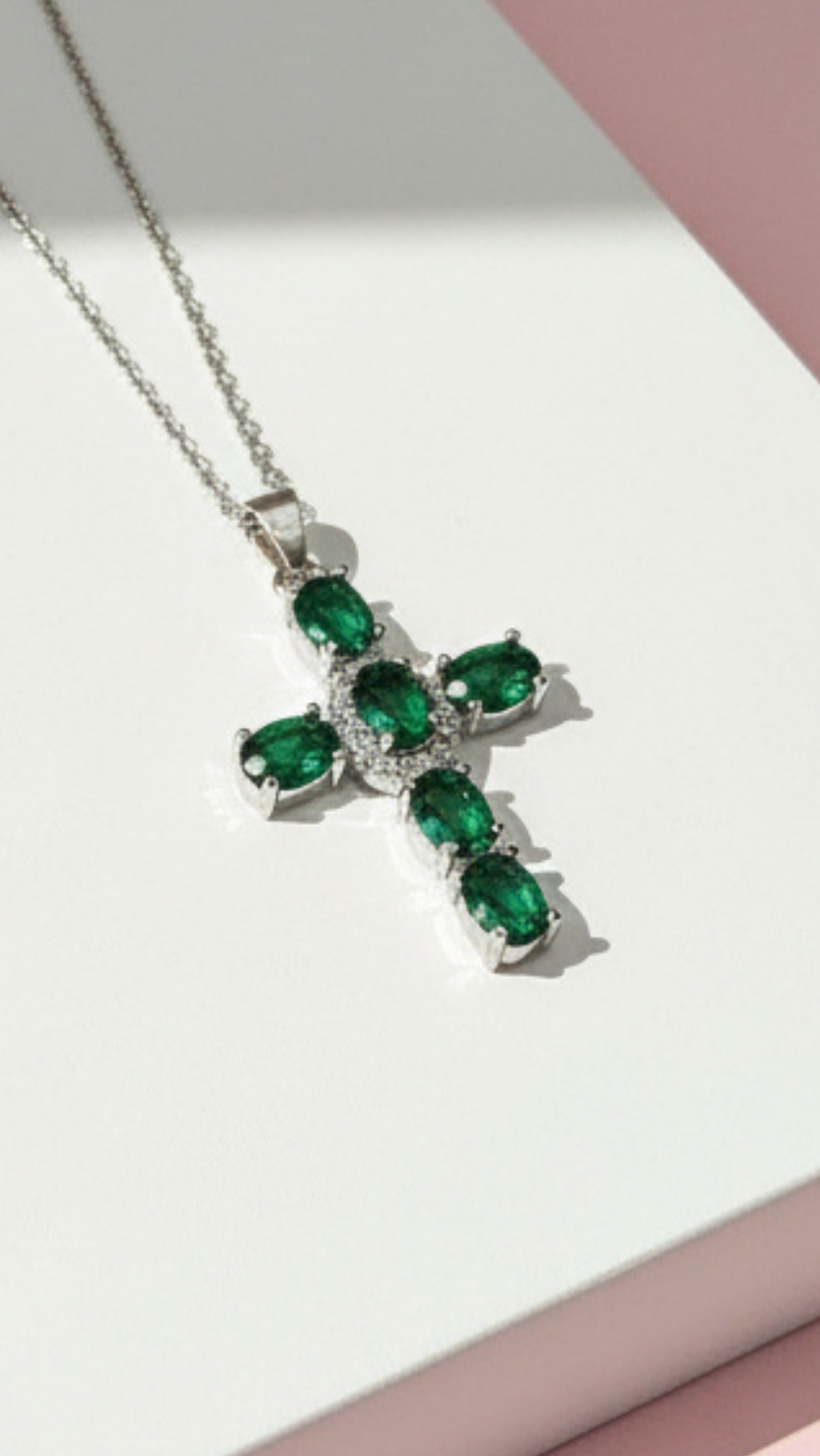 Cross-shaped pendant with green gemstones on a white surface