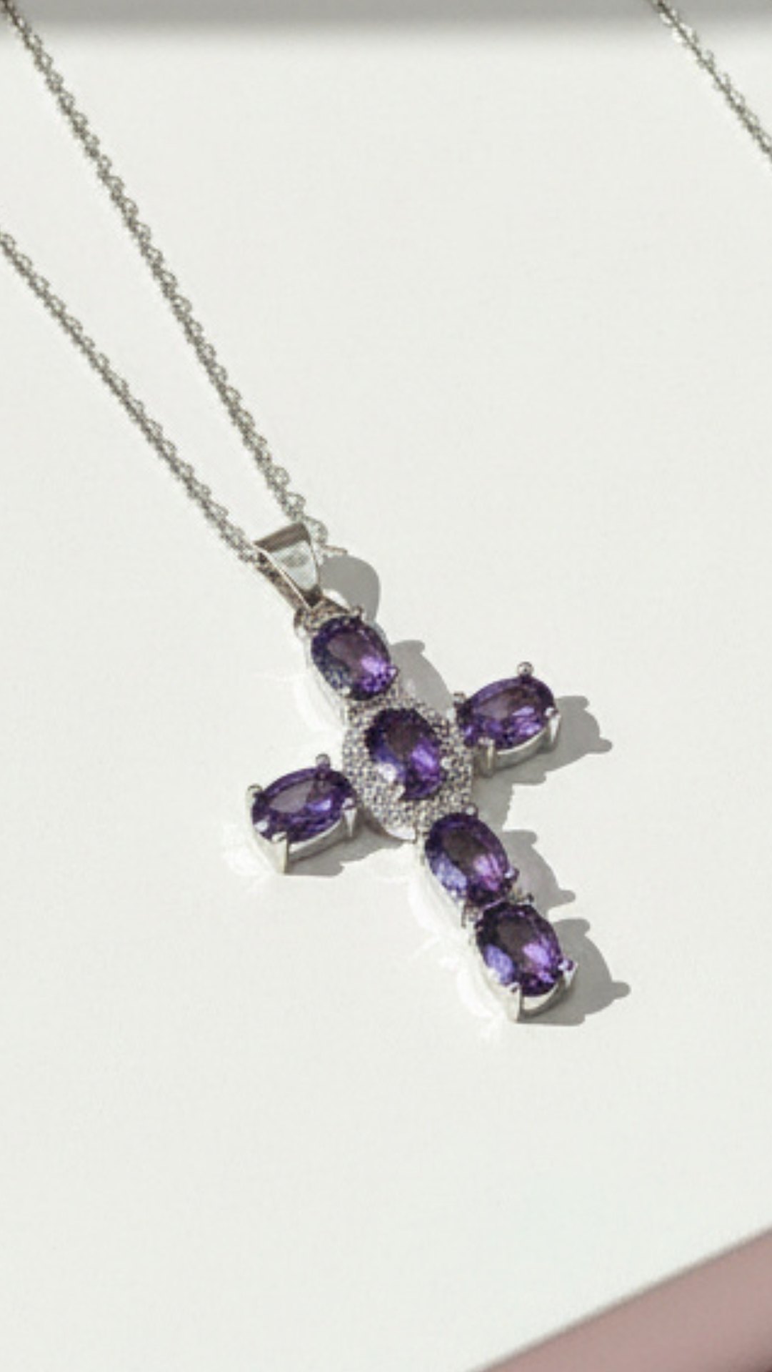 Cross-shaped pendant with light purple crystals displayed on a white surface