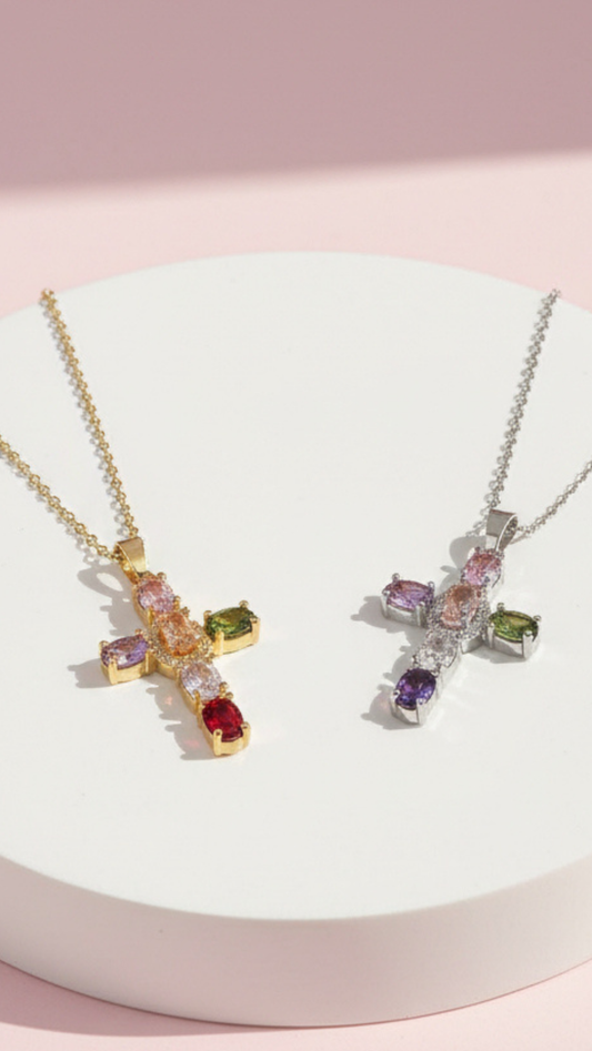 Multicolor cross pendants displayed on a white surface against a pink background