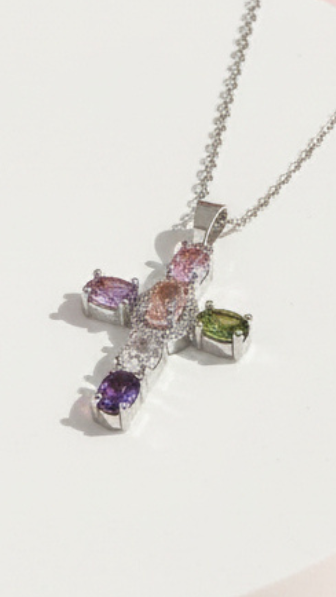 Cross pendant with multicolor stones displayed on a white surface