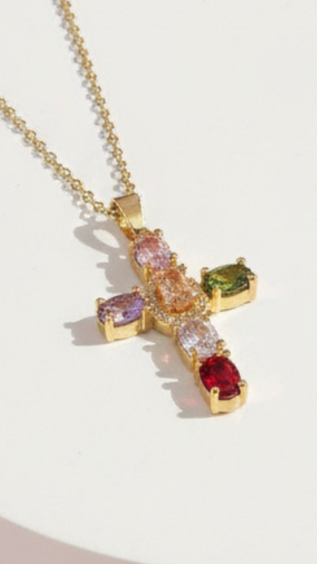 Gold cross necklace with colorful gemstones on a light background