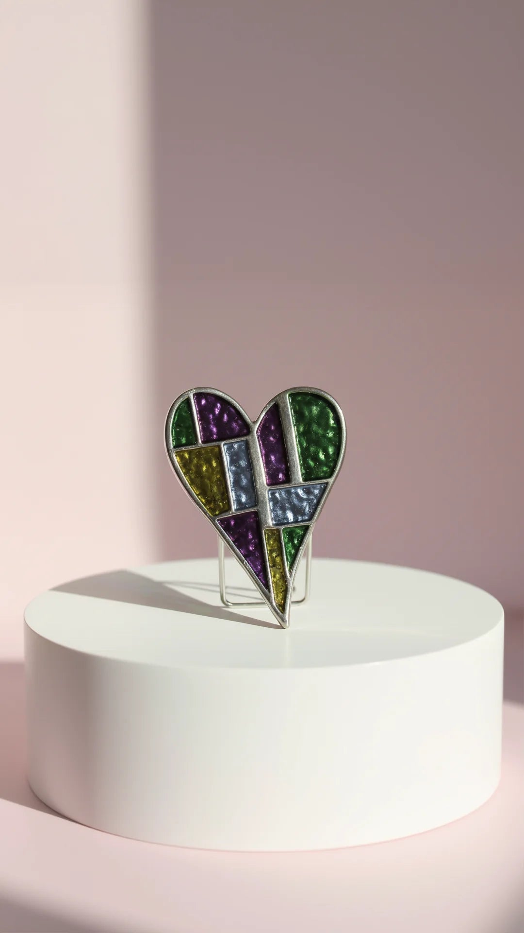 Heart-shaped brooch on a white pedestal against a light pink background