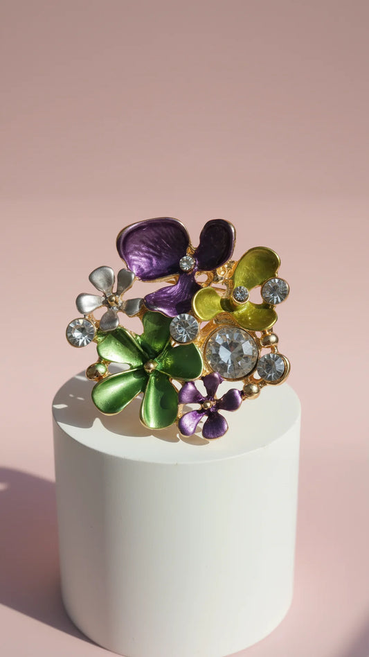 Decorative brooch with floral and gemstone design on a white pedestal against a pink background